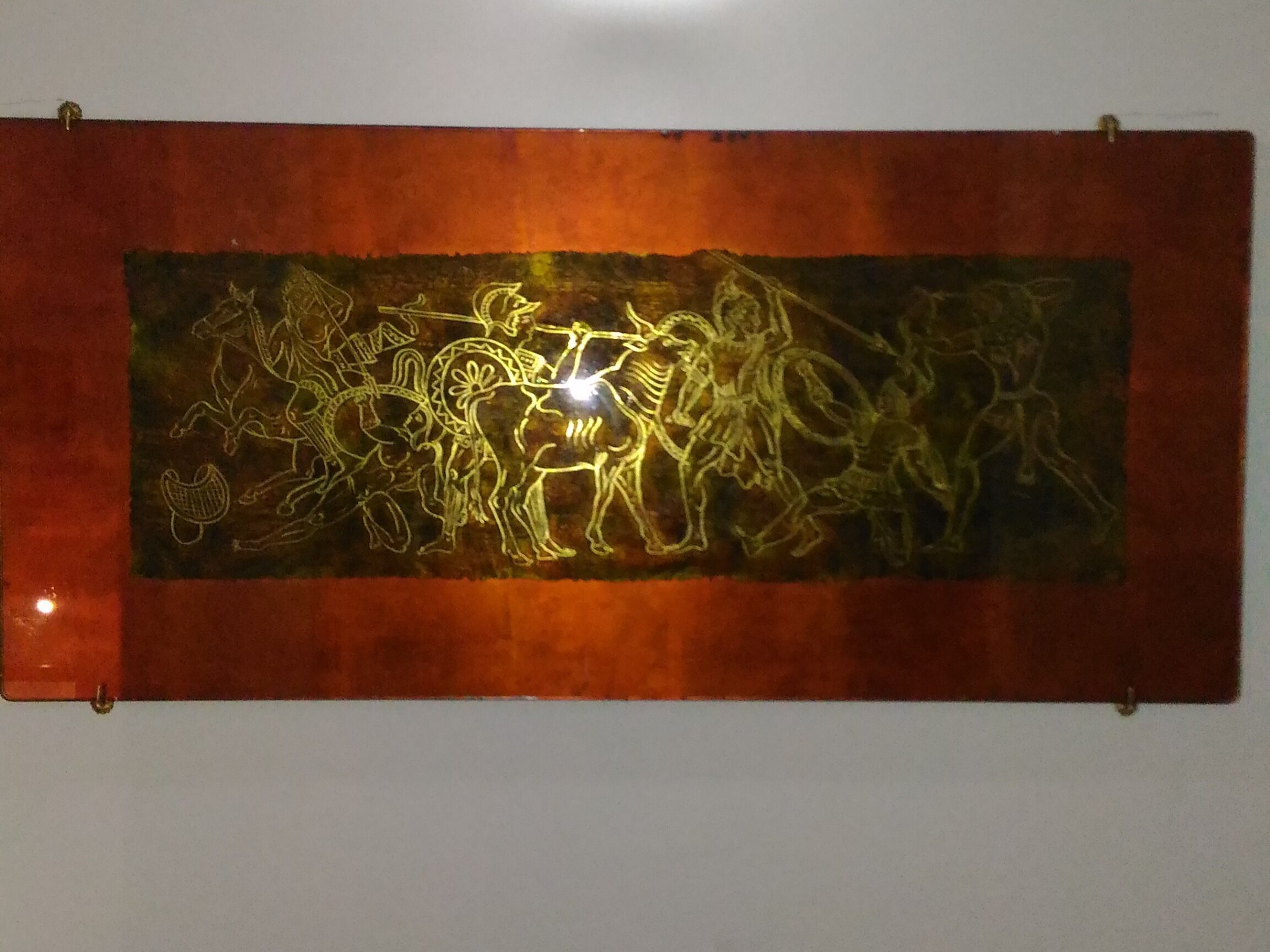 A wall-mounted artwork depicting a dynamic scene with figures and horses.
