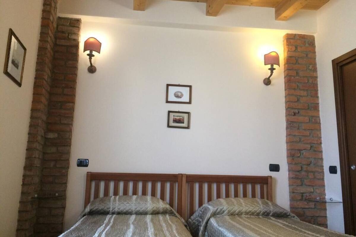 A room with two beds, brick walls, and two wall-mounted lamps.