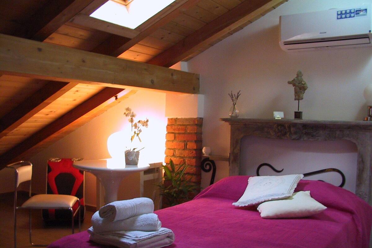 A cozy room with a bed, a chair, a small table, and a fireplace.
