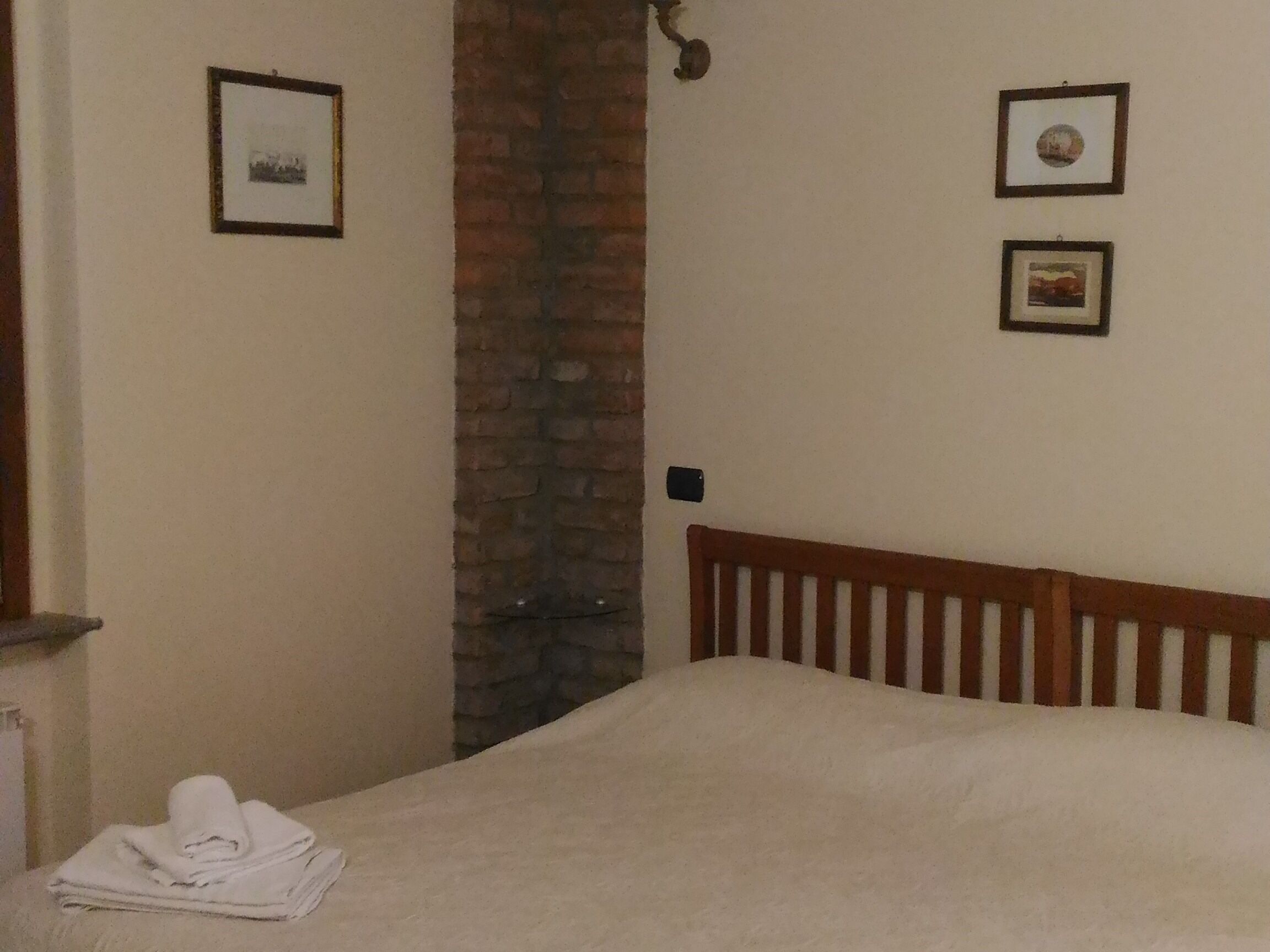 A bedroom with a wooden bed, a brick wall, and two framed pictures on the wall.