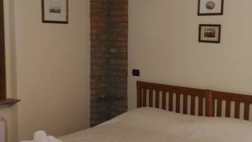 A bedroom with a wooden bed, a brick wall, and two framed pictures on the wall.