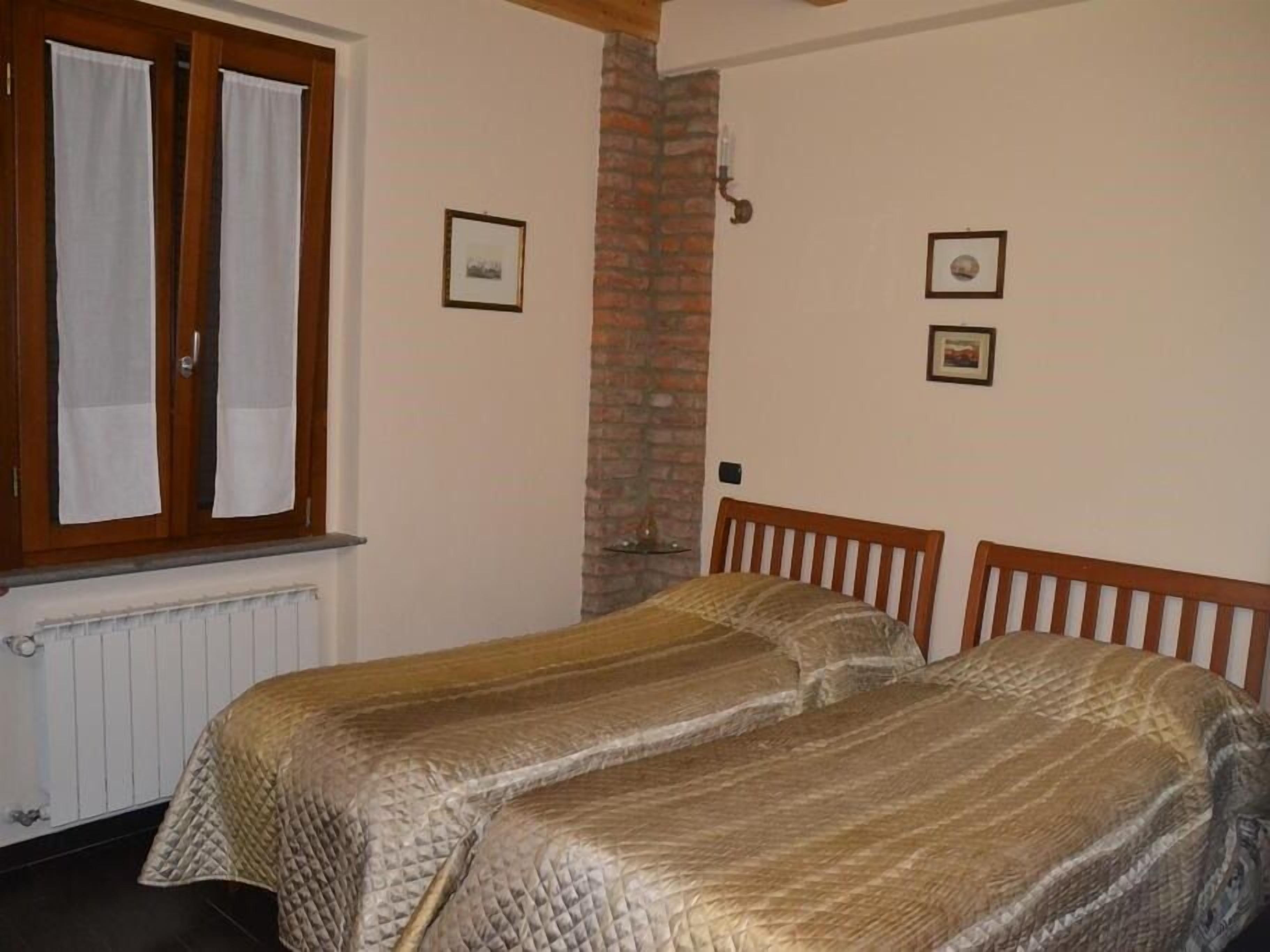 A room with two single beds, a brick wall, and a window with curtains.