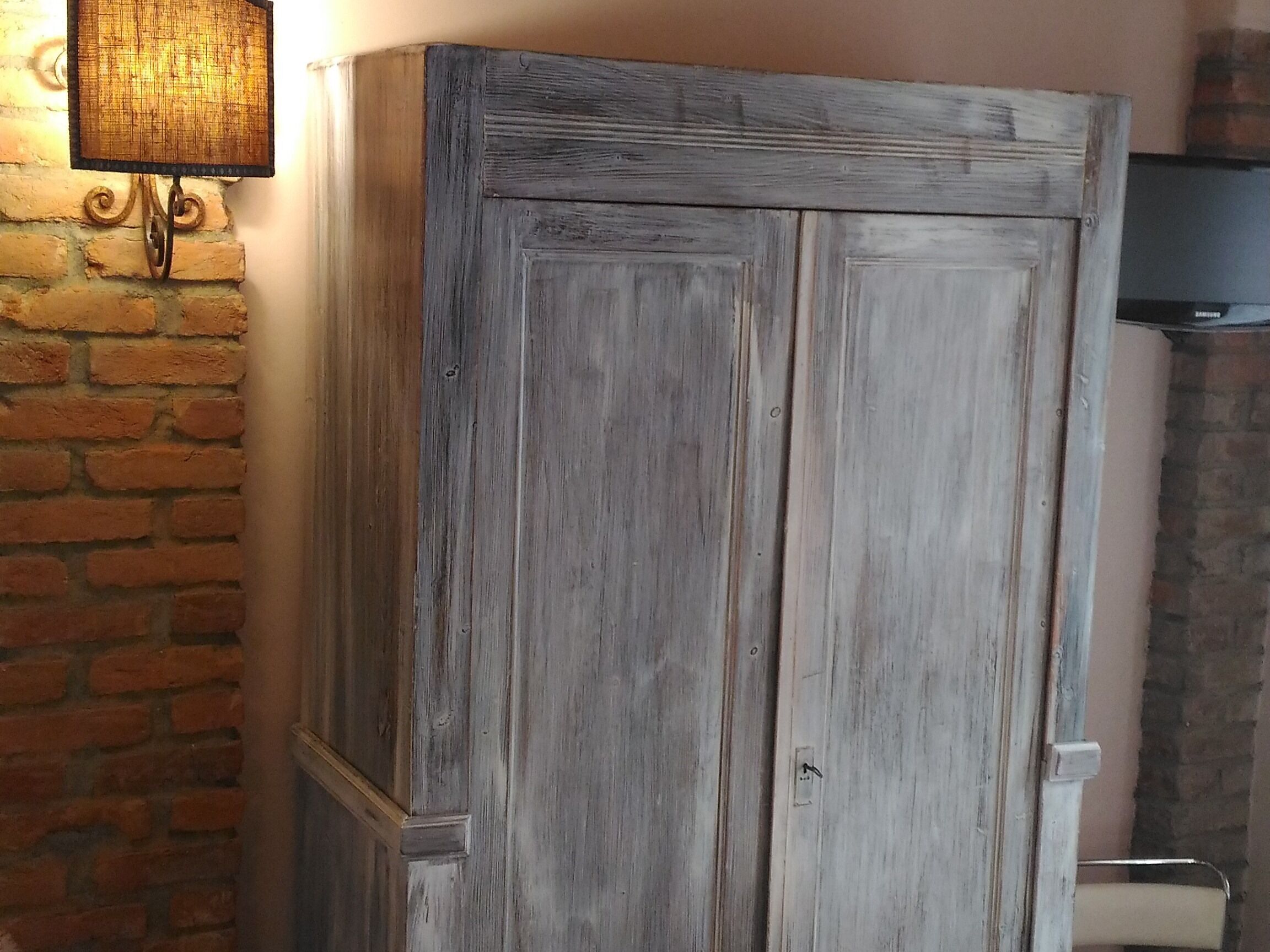 Un'armadietto di legno rustico con una maniglia in metallo, una parete in mattoni e una lampada fissata alla parete.