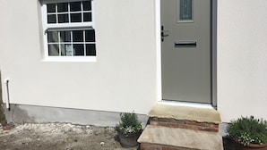 A white building with a grey door, a window, and a small brick step leading to the door. - White House Cottages (Durham)
