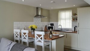 A compact kitchen with white cabinetry, a central island, and a dining area with white chairs. - White House Cottages (Durham)