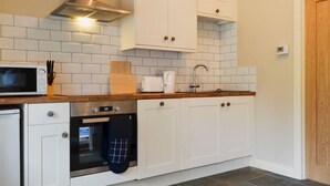 A compact kitchen with white cabinets, a microwave, an oven, and a sink. - White House Cottages (Durham)