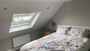 Ein Schlafzimmer mit Dachfenster, einem Bett mit floralem Bettzeug, einem Nachttisch mit Lampe und einer Heizung.