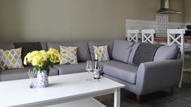 A modern living room with a grey sofa, white coffee table, and a vase of yellow flowers. - White House Cottages (Durham)