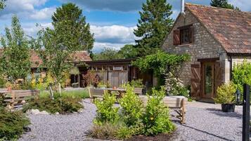 A rustic stone building with a chimney, surrounded by gravel paths and wooden benches.