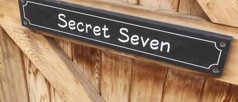 A black sign with white lettering on a wooden fence.