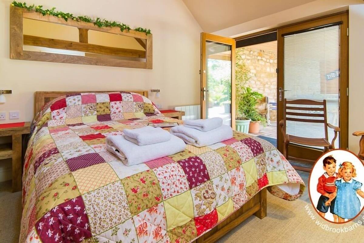 Een slaapkamer met een houten bed, een quilt, een nachtkastje, een kamerplant en uitzicht op het landschap door een glazen deur.