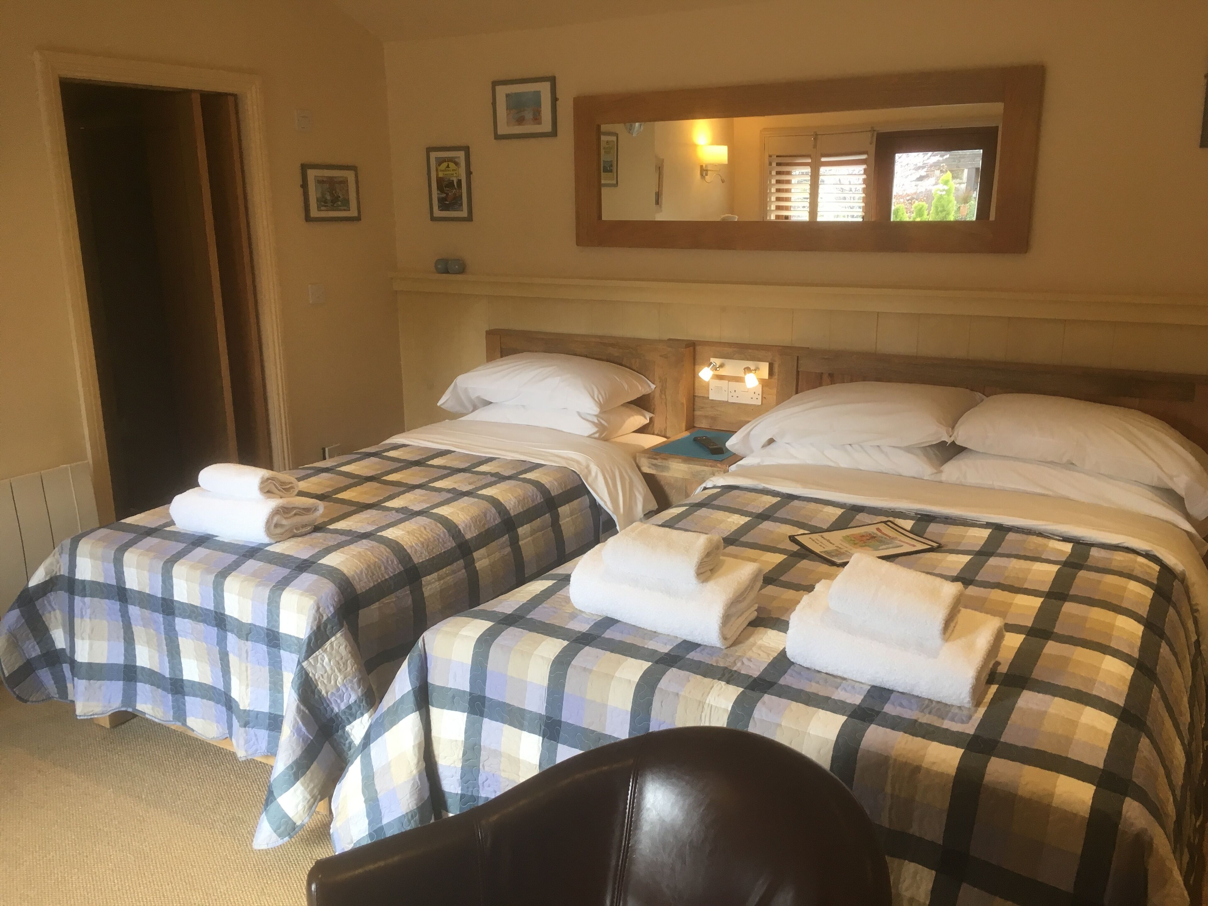 A hotel room with two beds, each with a checkered bedspread and white pillows. There is a wooden headboard, a nightstand with a lamp, and a mirror on the wall.