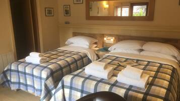 A hotel room with two beds, each with a checkered bedspread and white pillows. There is a wooden headboard, a nightstand with a lamp, and a mirror on the wall.