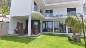 A modern two-story house with a flat roof, large glass windows, and a balcony.