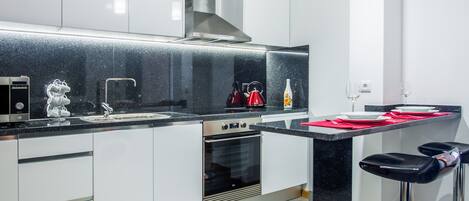 Une cuisine moderne avec des meubles blancs, un plan de travail noir, des appareils en acier inoxydable et un tabouret de bar.