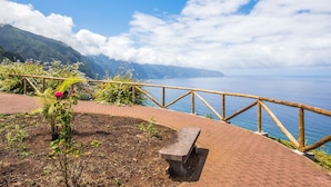 A paved walkway with a bench, surrounded by a wooden railing, overlooking a body of water and mountains.