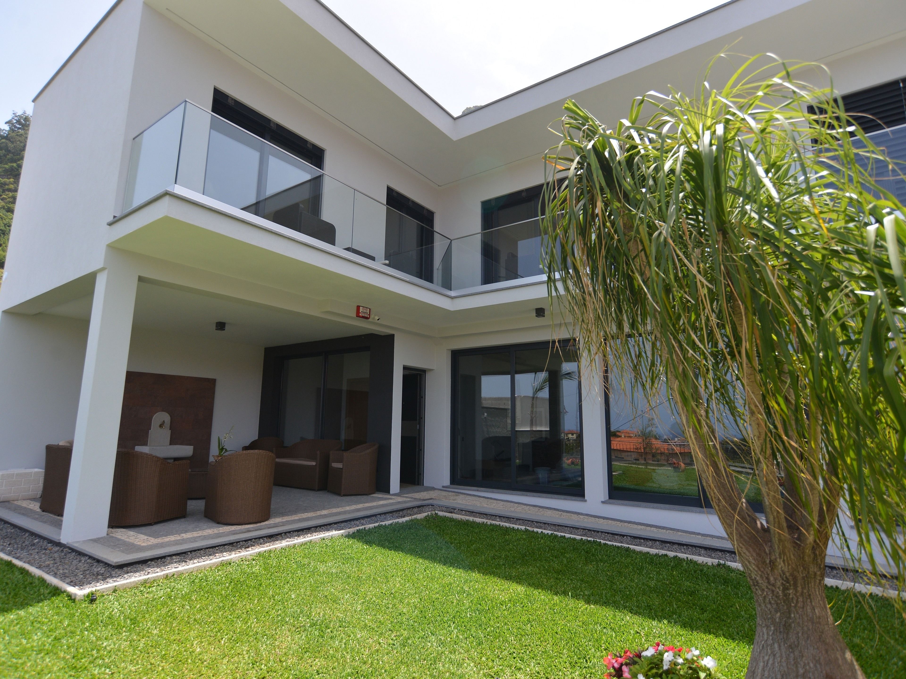 Une maison moderne à deux étages, dotée d’un balcon, d’un petit jardin et d’un arbre.