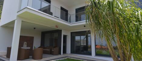 Une maison moderne à deux étages, dotée d’un balcon, d’un petit jardin et d’un arbre.