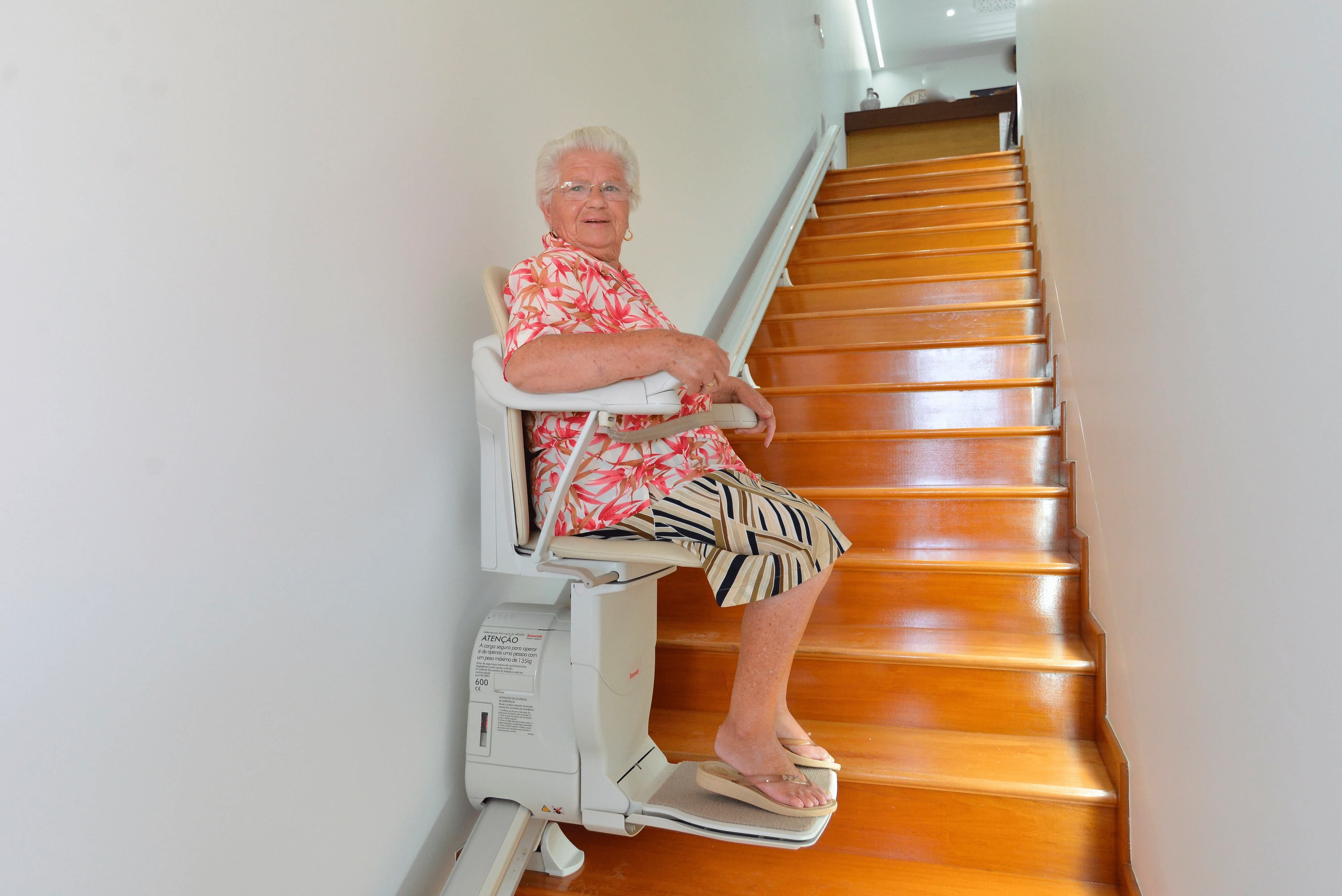 A person seated on a stair lift, ascending a wooden staircase.