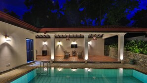 A swimming pool with a tiled deck, a covered seating area with chairs, and a stone wall. - Satiana Villa Tangalle (Tangalle)