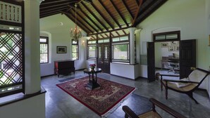A spacious room with a high ceiling, a large window, a traditional chair, a table with a vase, and a patterned rug. - Satiana Villa Tangalle (Tangalle)
