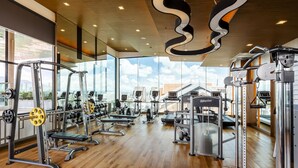 A modern gym with various exercise equipment, large windows, and a wooden floor. - Anta Residence Self-service Apartment (Chiang Mai)