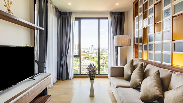 A modern living room with a flat-screen TV, a sofa, a coffee table, and a large window with curtains. - Anta Residence Self-service Apartment (Chiang Mai)