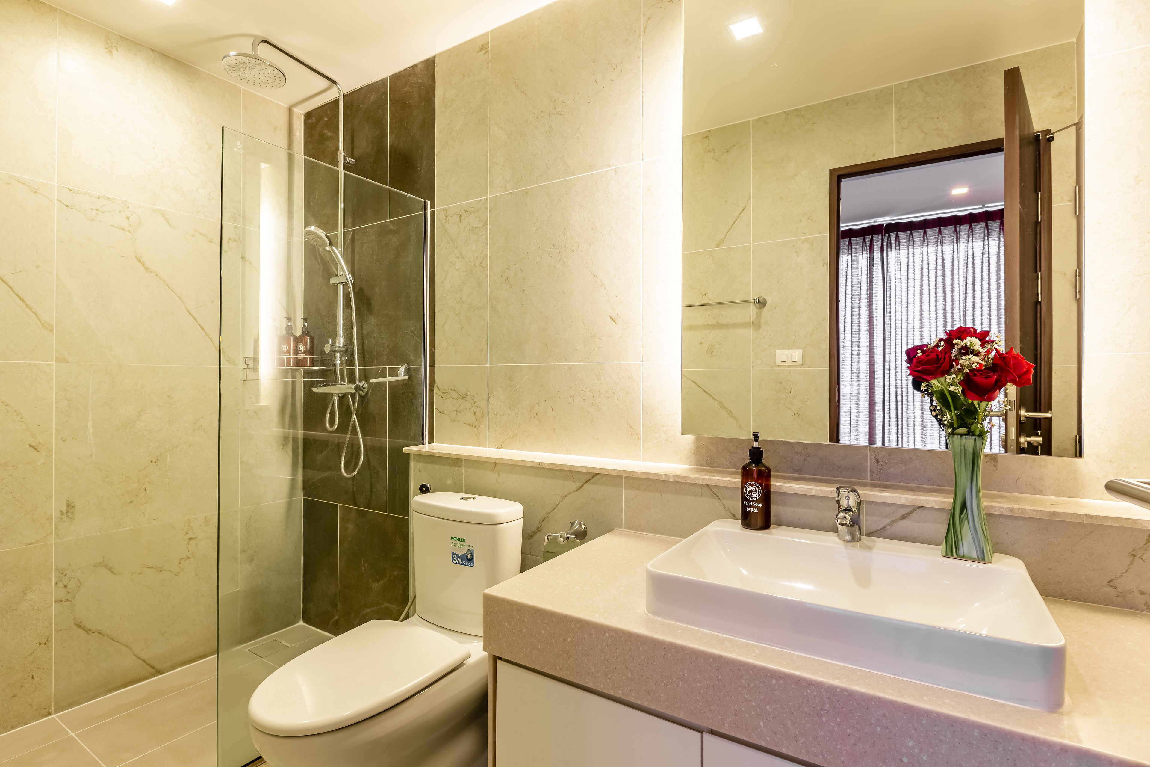 A modern bathroom with a glass-enclosed shower, a white toilet, and a sink with a vase of flowers.