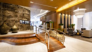 A modern lobby with a marble wall, wooden staircase, and contemporary furniture. - Anta Residence Self-service Apartment (Chiang Mai)
