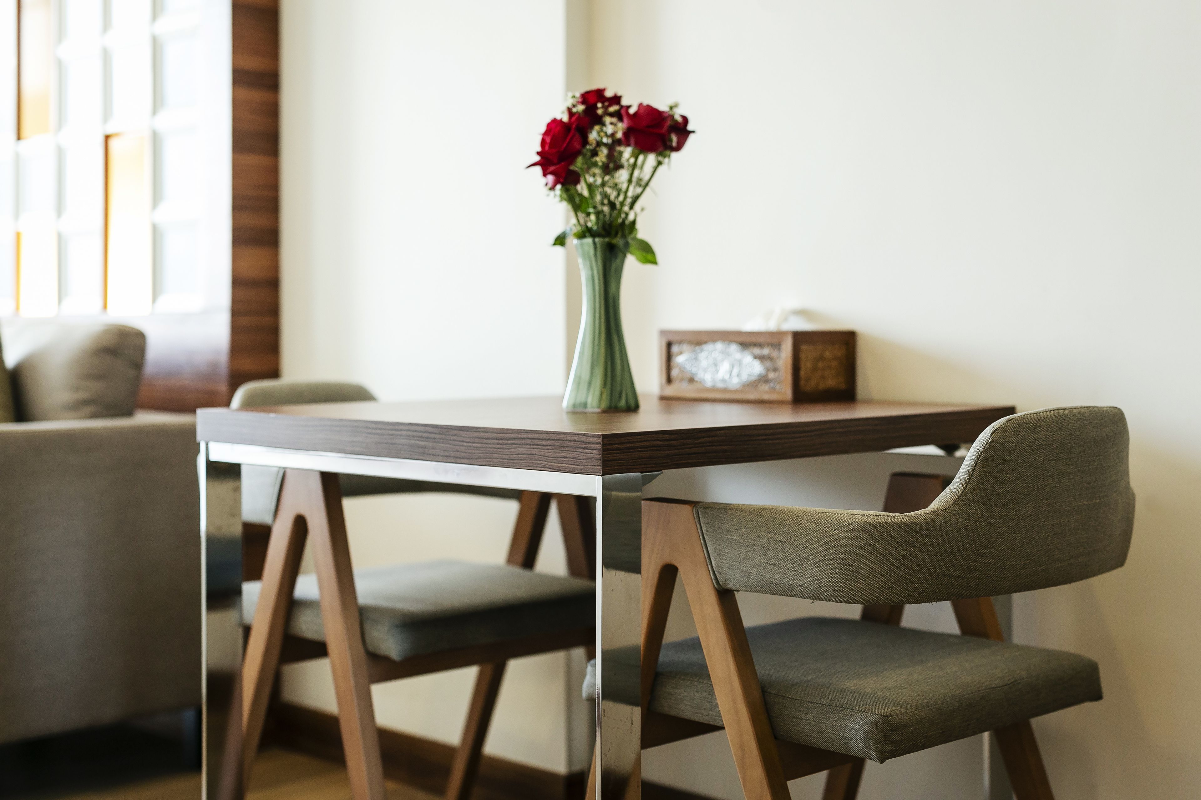 Een eettafel met een vaas rode bloemen, een lijst met foto en een stoel met een grijze kussen.