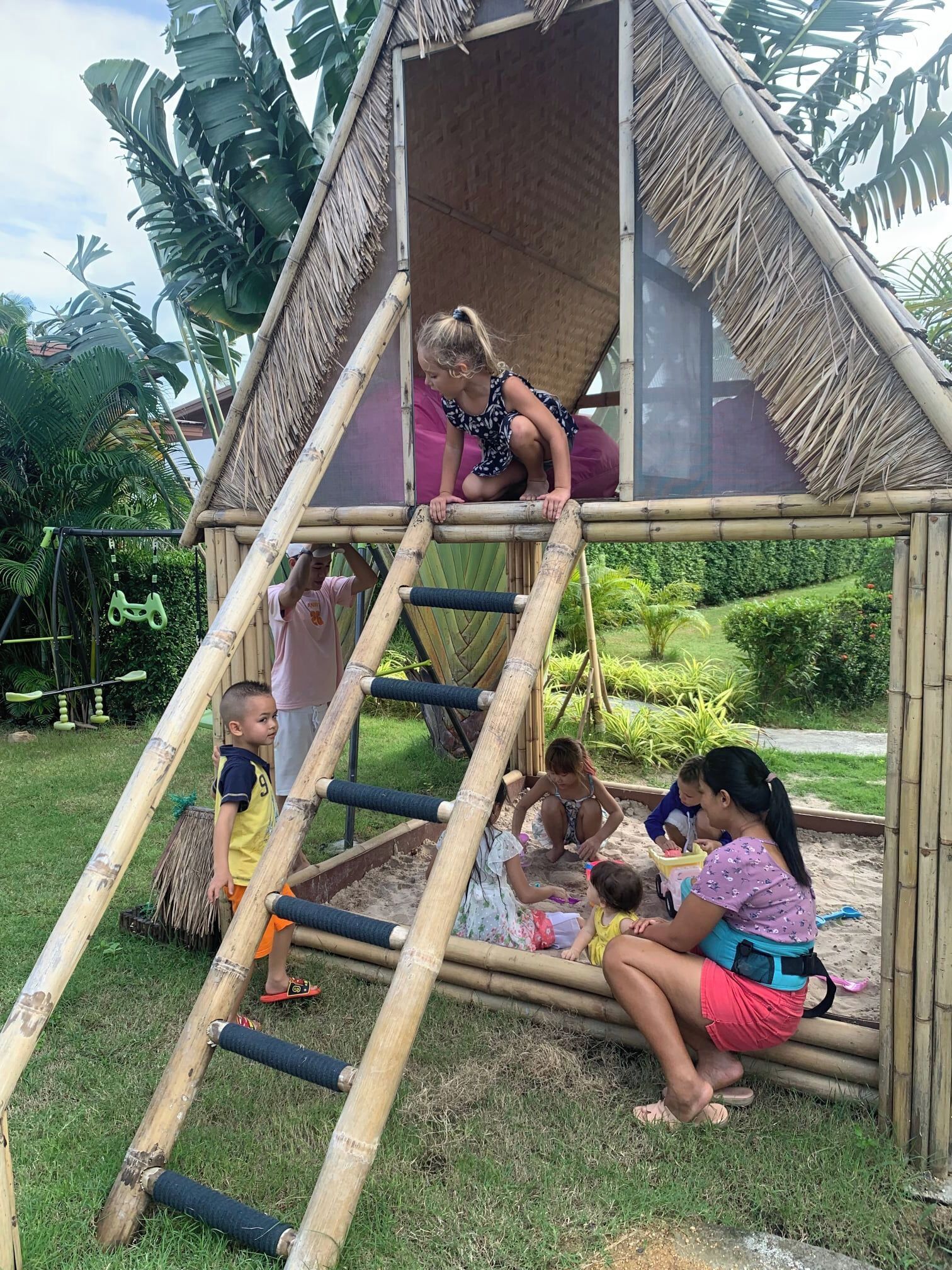 Estructura de juego de bambú con una escalera y un tobogán, rodeada de follaje.