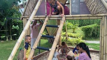 Estructura de juego de bambú con una escalera y un tobogán, rodeada de follaje.
