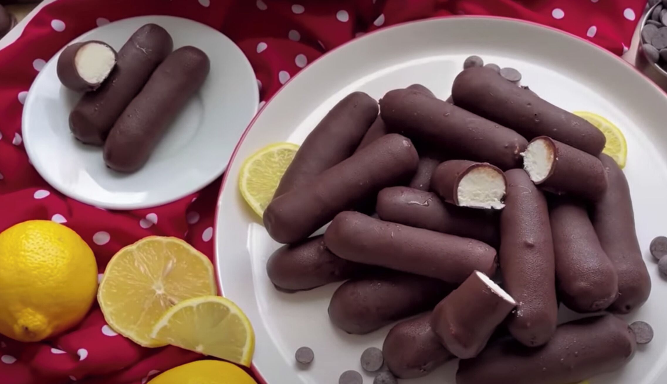 A plate of chocolate-covered treats with lemon slices and a lemon on a red polka-dotted cloth.