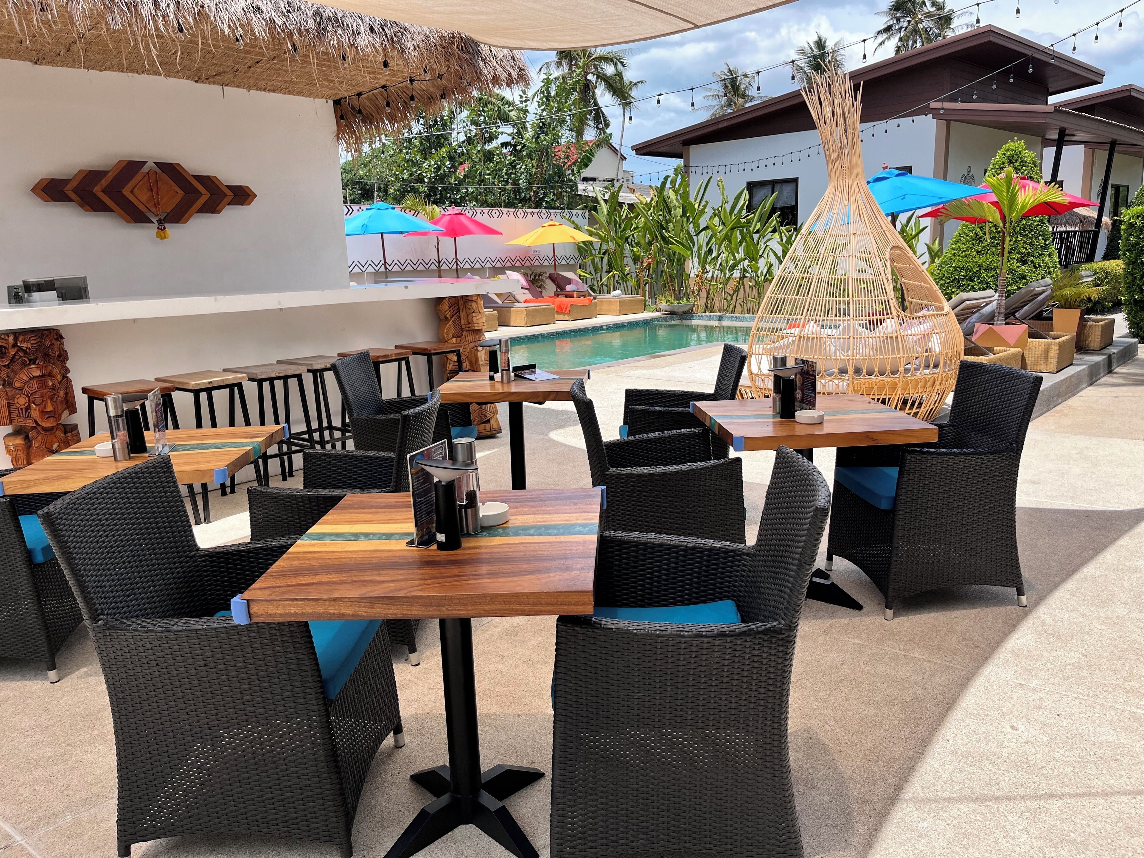 Un espace extérieur aménagé pour les repas, avec des meubles en osier, une piscine et des parasols.