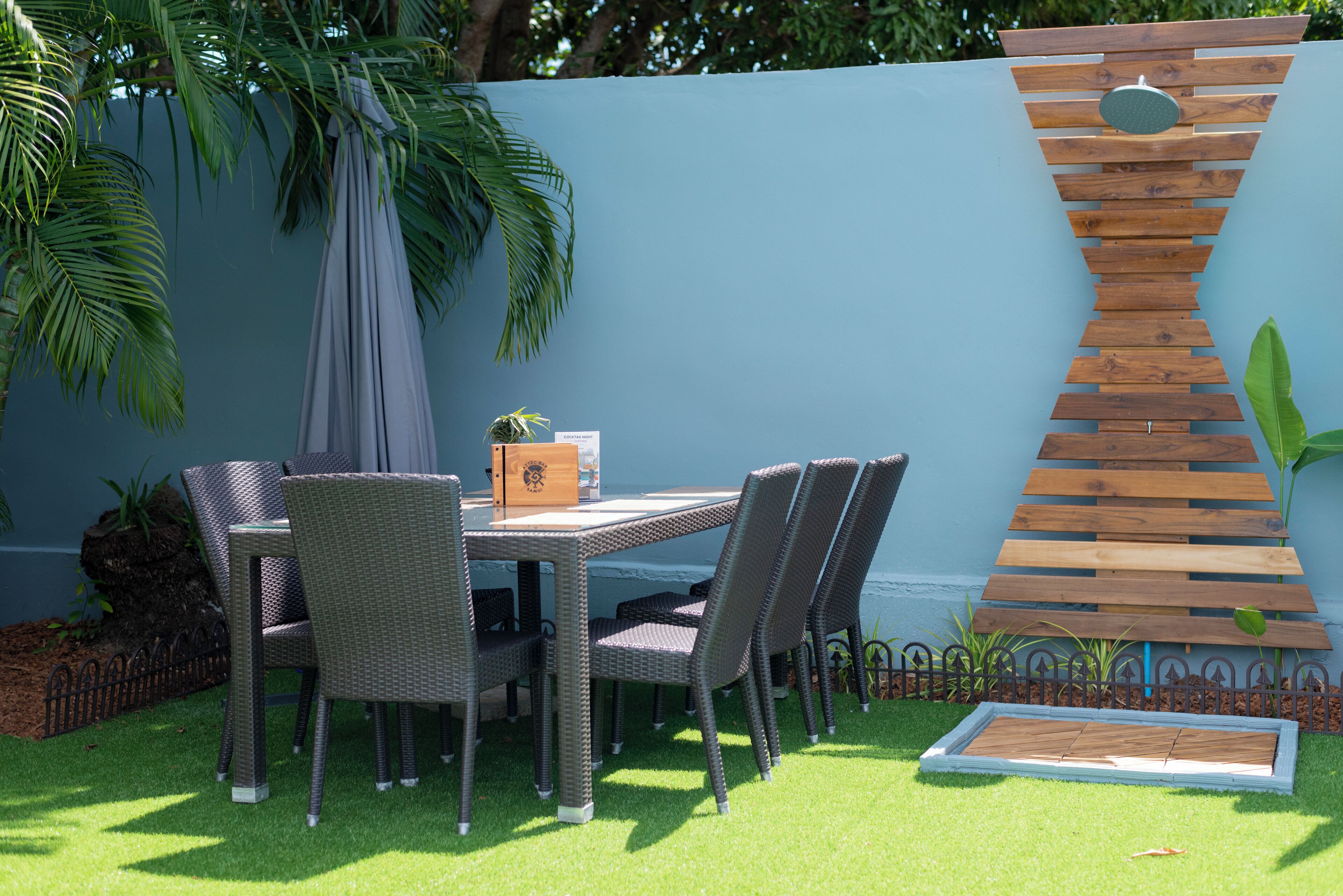A patio with a table and chairs, a wooden wall feature, and a small plant.