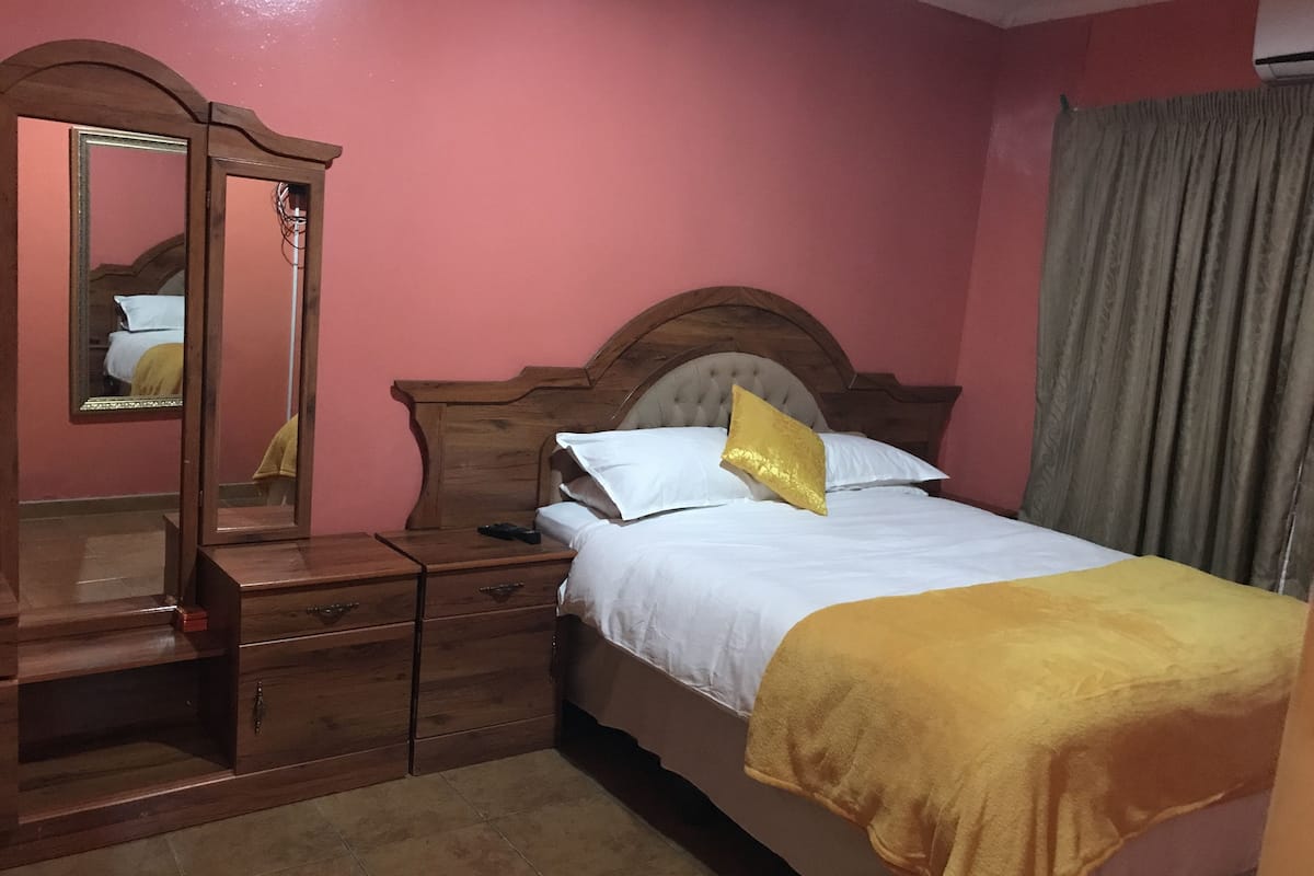 Ein Schlafzimmer mit einem hölzernen Bett, einem Nachttisch, einer Kommode und einem Spiegel.