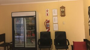 A room with a refrigerator stocked with beverages, two black chairs, a red cushion, and a wall clock. - Essence of Africa Guesthouse (Windhoek)