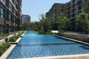 Piscina com piso em azulejo, cercada por vegetação e edifícios modernos.