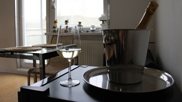 A dining area with a table, chairs, a wine glass, and a metal pot. - Apartmán Relax so saunou a jakuzzi (Namestovo)