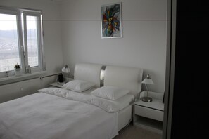 Une chambre à coucher avec un grand lit, deux tables de chevet, une fenêtre avec des stores et un tableau accroché au mur.
