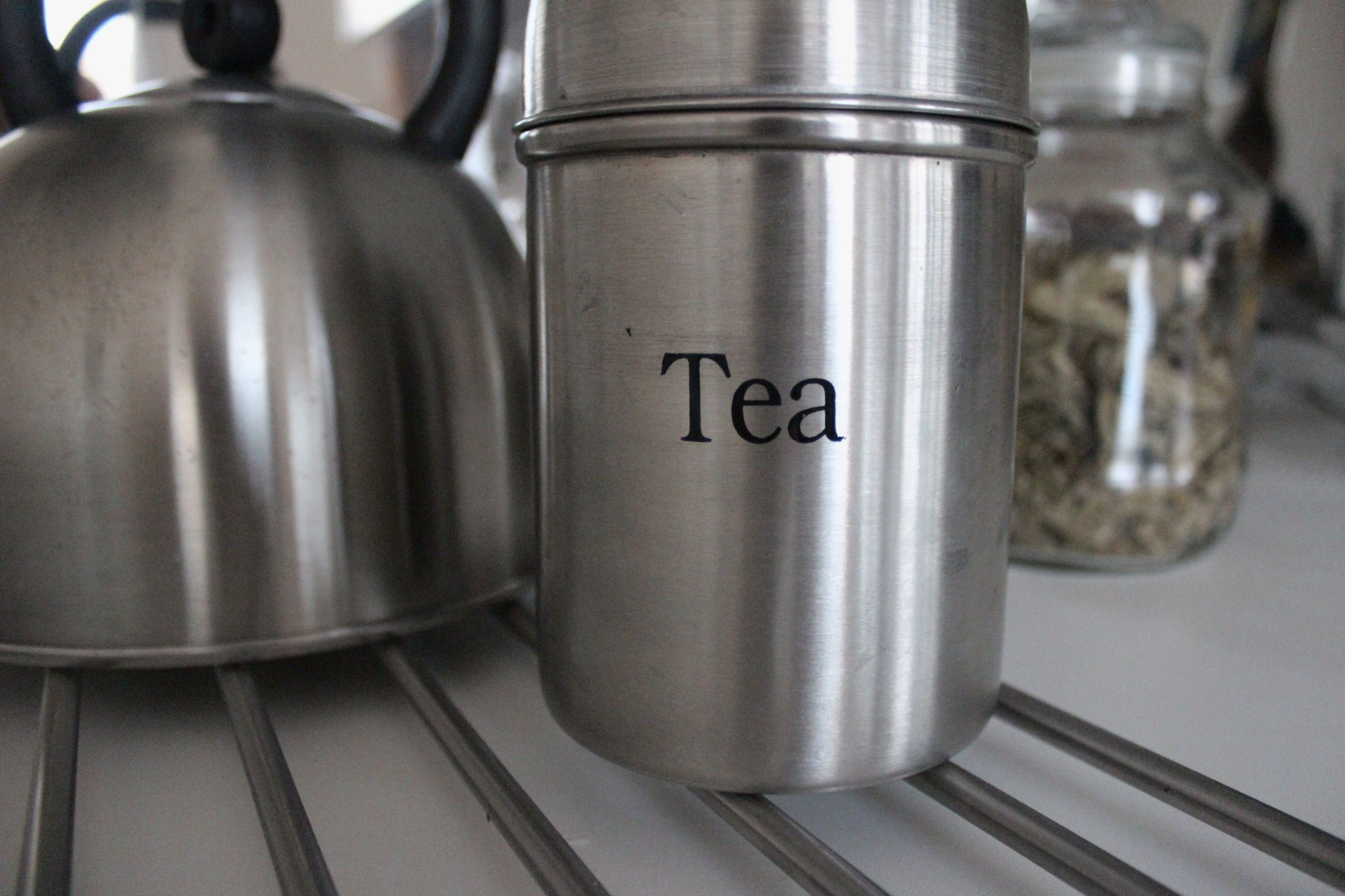 A stainless steel container labeled "Tea" on a kitchen shelf.