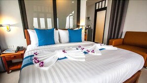Un lit bien fait, avec des oreillers blancs et bleus, une table de chevet en bois avec un téléphone, et un canapé marron dans une chambre d’hôtel.