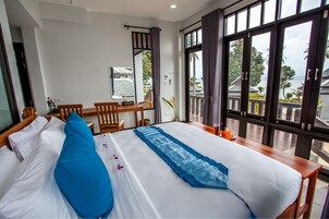 Habitación de hotel con una cama grande, un escritorio de madera y vistas al mar a través de amplios ventanales.