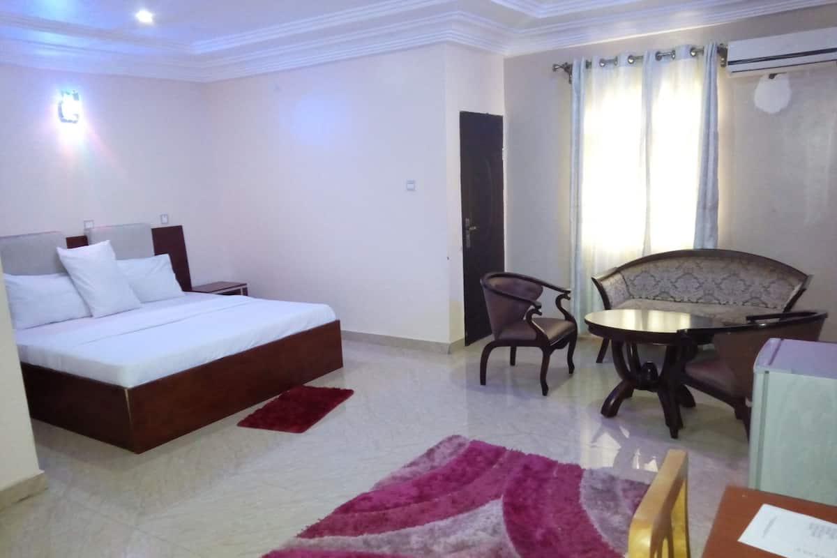 Quarto de hotel com uma cama, uma mesinha com cadeiras, um tapete vermelho e uma janela com cortinas.