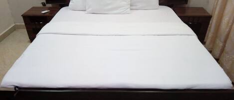 A neatly made bed with white bedding and pillows, a wooden headboard, and a nightstand with a remote control.