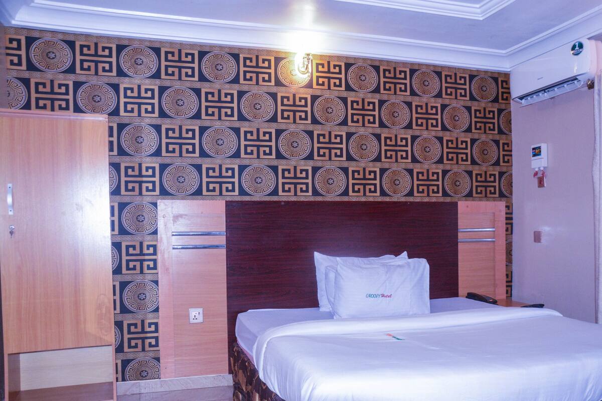 Quarto de hotel com uma cama, um guarda-roupa de madeira e um papel de parede estampado.