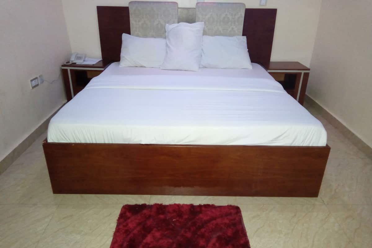 Quarto de hotel padrão com uma cama de solteiro, mesa de cabeceira, telefone e tapete vermelho.