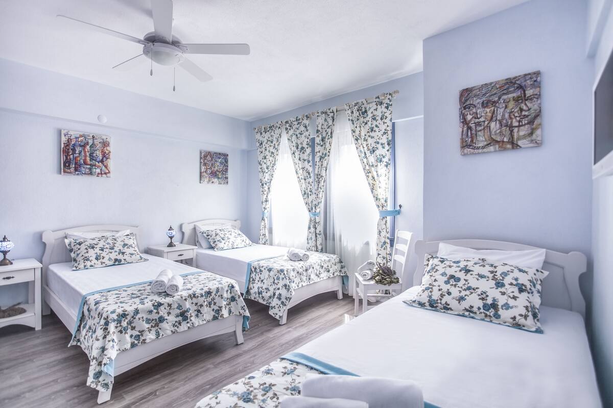 A hotel room with two single beds, a ceiling fan, floral curtains, and artwork on the walls.