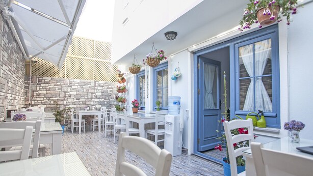 An outdoor dining area with white tables and chairs, blue doors, and hanging flower baskets. - Bozcaada Basak Konukevi (Bozcaada)