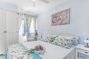 A bedroom with a bed, a nightstand, a ceiling fan, a window with curtains, and a painting on the wall. - Bozcaada Basak Konukevi (Bozcaada)